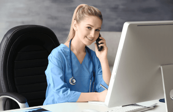 Smiling female nurse asking the desk phone as she checks her email correspondences 
