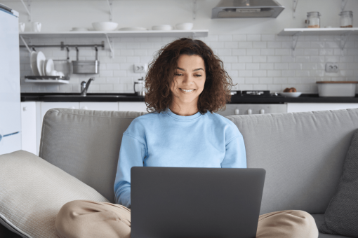 woman with a blue jumper sending emails on her laptop as she sits on her couch